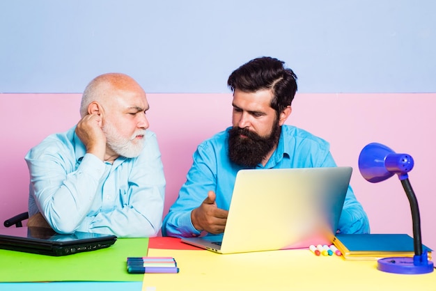 Employees sit at office desk look at laptop screen cooperating in office Businessman read news in internet Two colleagues working together at office on color background