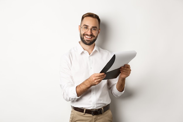 Employer looking satisfied at CV, reading document and smiling, standing over white background.