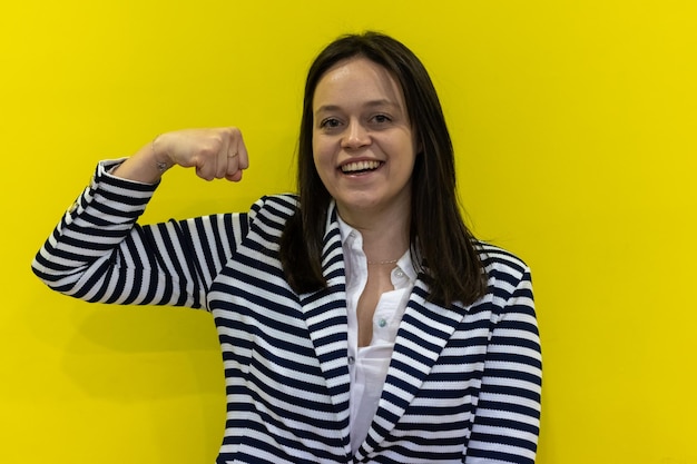 An empowered woman showing her bicep on a yellow background