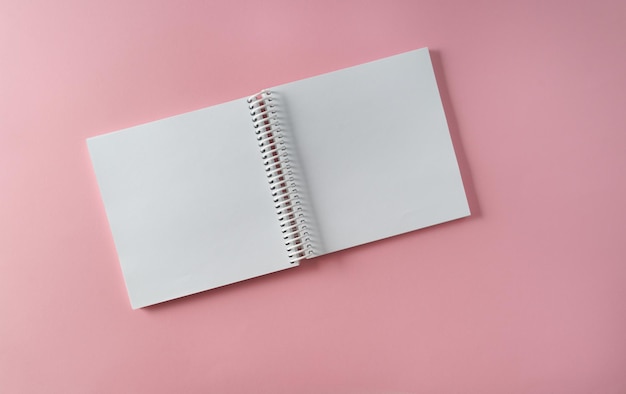 An empty A4 notebook in expanded form on a pink paper background top viewmockup