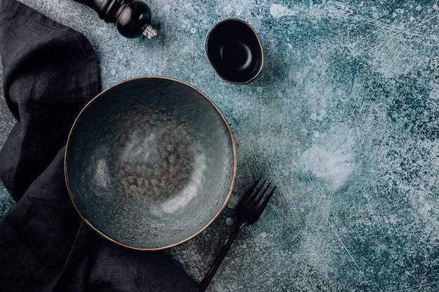 Empty black bowl with napkin linen napkin fork and gravy bowl over old gray background