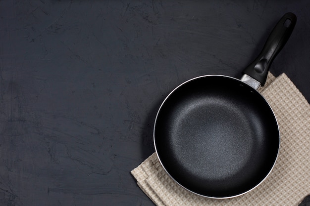 Empty black frying pan with kitchen towel on black table.