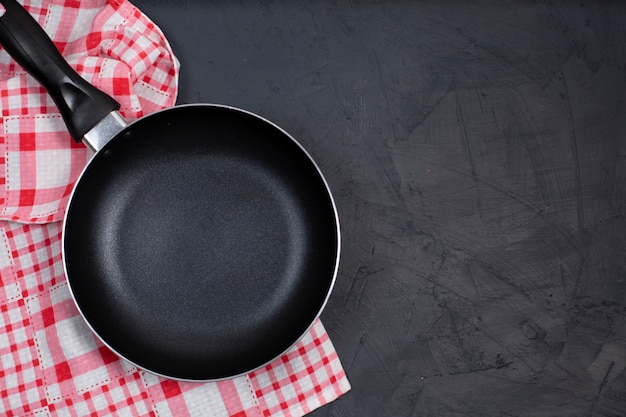 Empty black frying pan with kitchen towel on black table.