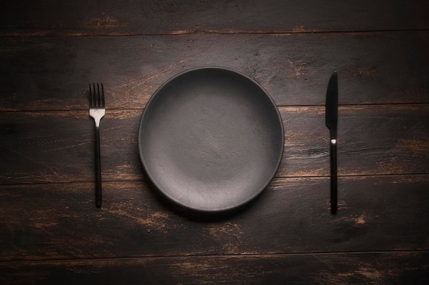 An empty black plate and cutlery on a wooden table top view