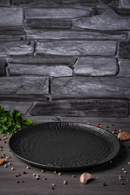 An empty black plate on a grey background with spices and herbs Empty copy space Home dinner cooking