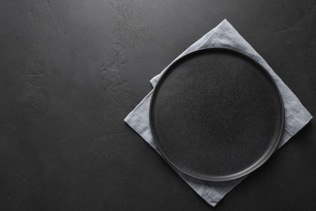 Empty black plate with lilac towel on black kitchen background Space for design View from above