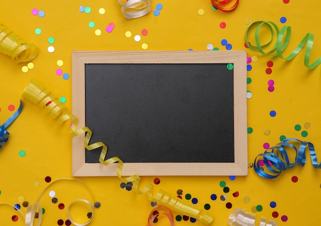 Empty blackboard with Colored streamer and confetti on yellow background Holiday birthday background