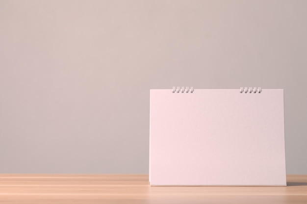 Empty blank page of paper desk calendar on the top of wooden table with grey color space wall