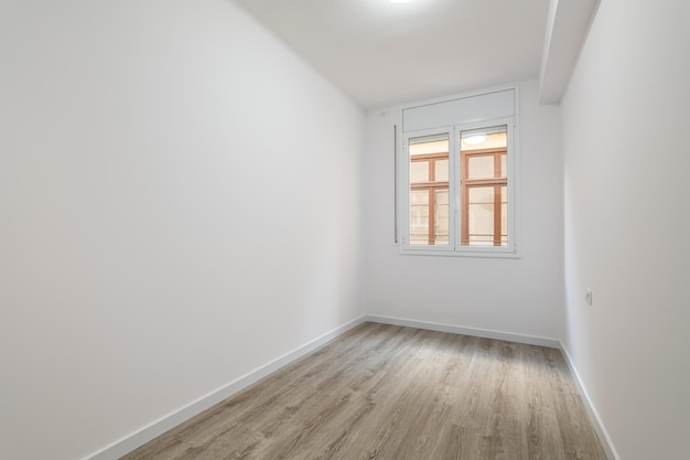 An empty bright room with a window in which the windows of a nearby house are visible external metal