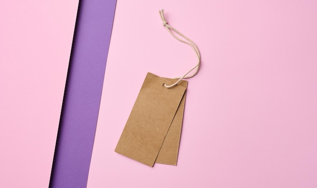 Empty brown tags on a rope pink background Price template top view