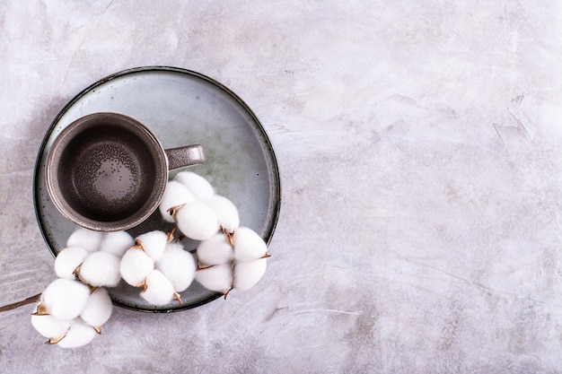 Empty ceramic mug and branch in cotton on a plate on a gray background top view