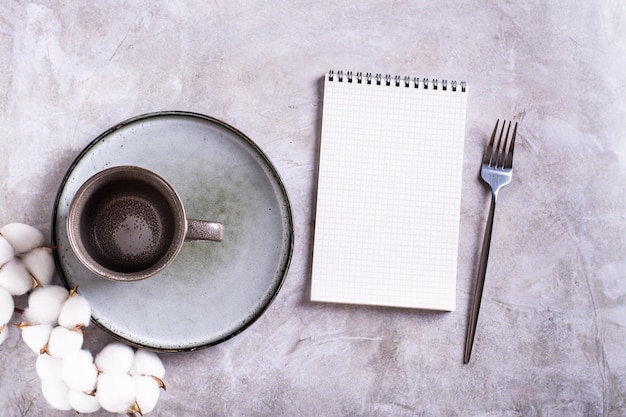 Empty ceramic mug plate cotton and blank open notebook on gray background top view