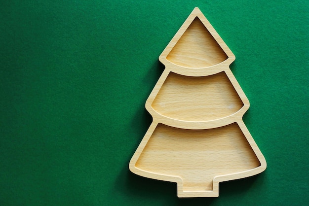 Empty Christmas or new year wood plate in in the shape of a Christmas tree on a green background Top view