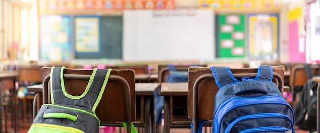 Empty classroom in elementary school with whiteboard and teacher's desk school bag hanging