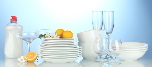 Empty clean plates glasses and cups with dishwashing liquidand lemon on blue background