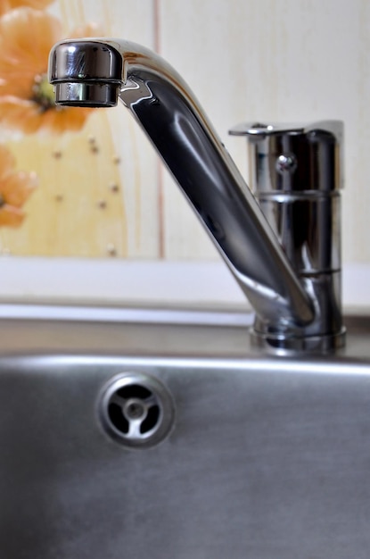 Empty clean silvery kitchen sink and water faucet close up