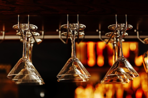 Empty clean upsidedown crystal martini glasses hanging from the bar in luxury restaurant Selective focus blurred colourful background