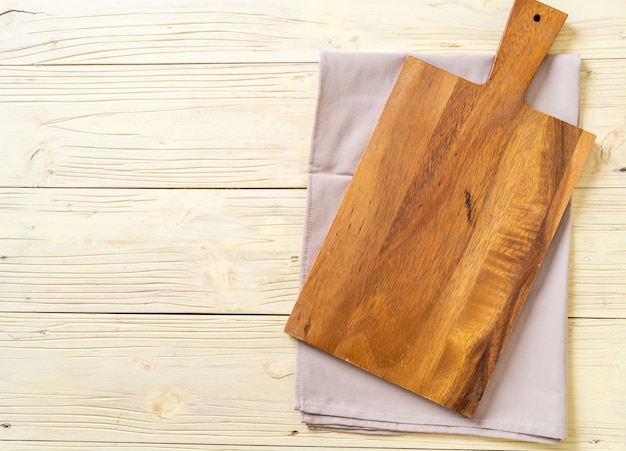 empty cutting wooden board with kitchen cloth on wooden background, top view