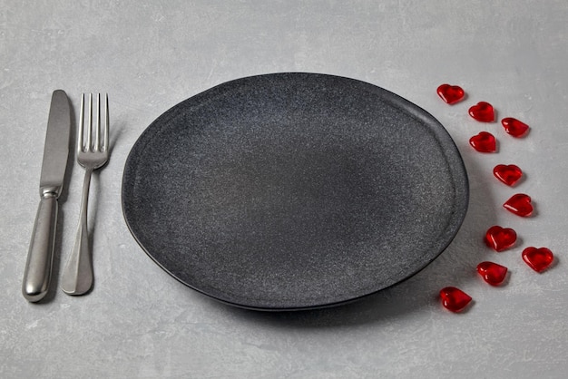 Empty dark plate with cutlery and red caramel hearts on a light concrete table Romantic menu Top view