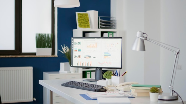 Empty desk with computer monitor showing financial statistics charts on screen. Nobody in startup business office with commercial data graphs and analysis for company development.