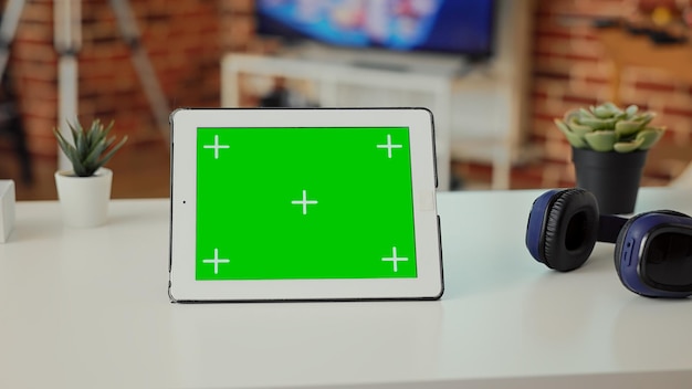 Empty desk with digital tablet showing green screen on display, used to work on modern technology at home. Isolated mockup template and chroma key background with copyspace screen on wireless device.