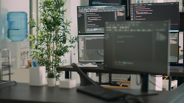 Empty desk with multiple monitors displaying server code and programming language, compiling in software developing agency office. System cloud computing online database algorithms.