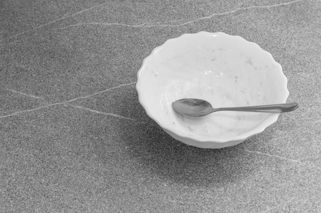 Empty dirty white plate with some dessert crumbs and a spoon on gray concrete background, top view, black and white, copy space