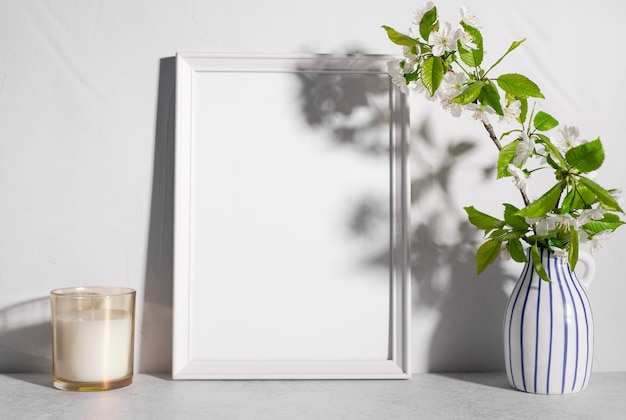 Empty frame mockup with tree blossoms in vase and scented candle