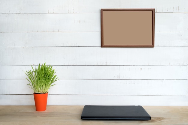 Empty frame on white wall. Closed notebook and green houseplant. Home workplace. Place for text