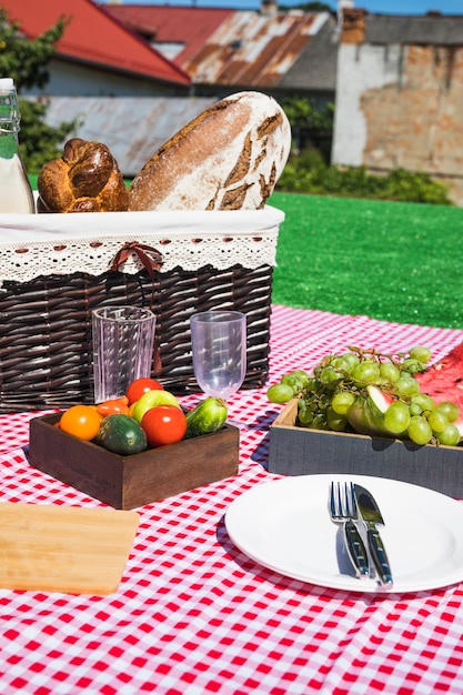 Empty glasses; cutlery; fruits and vegetables with picnic basket on blanket