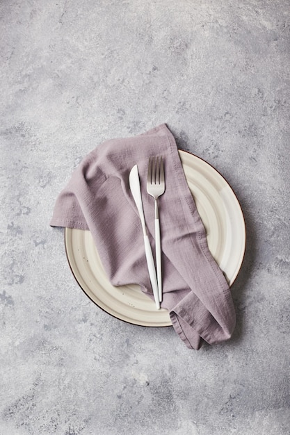 Empty gray plate with napkin and cutlery on gray background