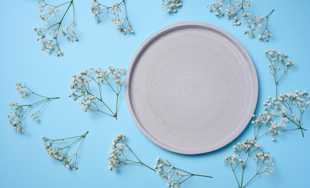 An empty gray round decorative plate on a blue background around a gypsophila branch