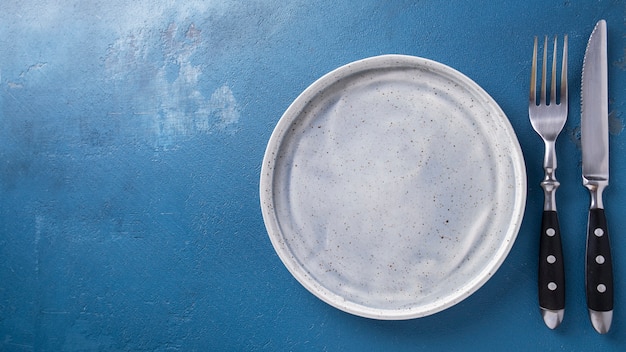 Empty grey plate  fork and knife on a blue surface. Top view.