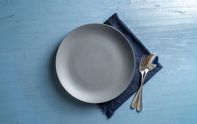 empty grey plate fork and spoon on light blue wooden table with dark blue tablecloth Top view Mock up