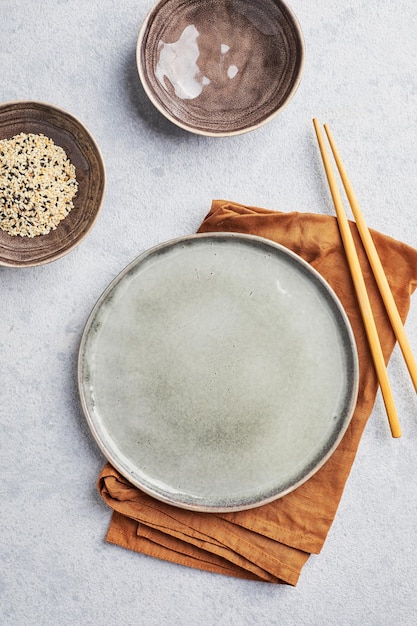 Empty grey round plate with chopsticks and linen napkin on gray background top view