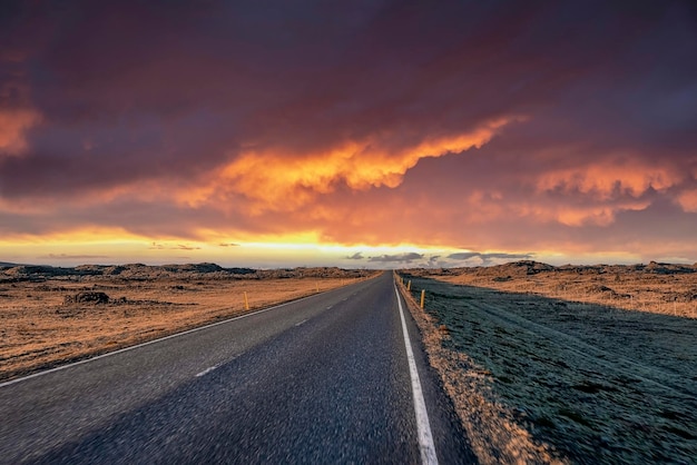 Empty highway amidst volcanic landscape against dramatic sky during sunset