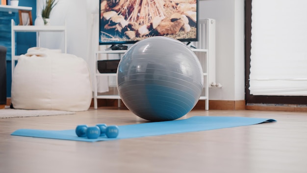 Empty living room with sport training equipment on floor. Nobody in space with fitness toning ball and dumbbells placed on yoga mat used to exercise for wellness and healthcare.