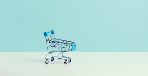 Empty miniature shopping cart on a blue background. Seasonal sale, copy space