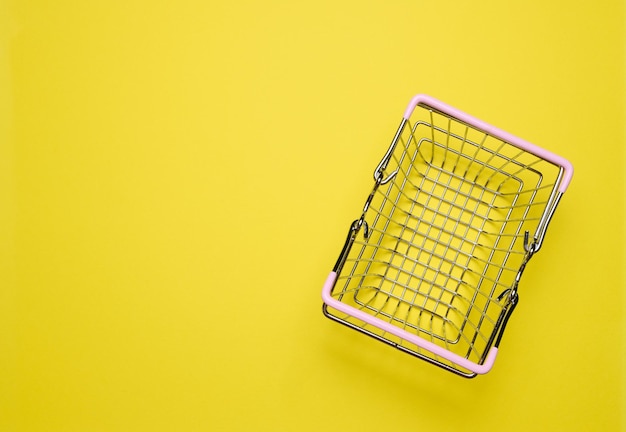 Empty miniature shopping cart on a yellow background top view representing the concept of shopping