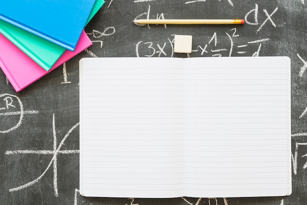 Empty notebook with pen and books on chalkboard