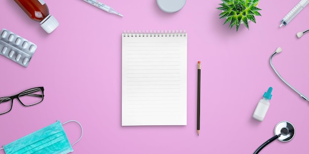 Empty notepad on hospital desk surrounded by medical equipment and medicines Top view flat lay composition