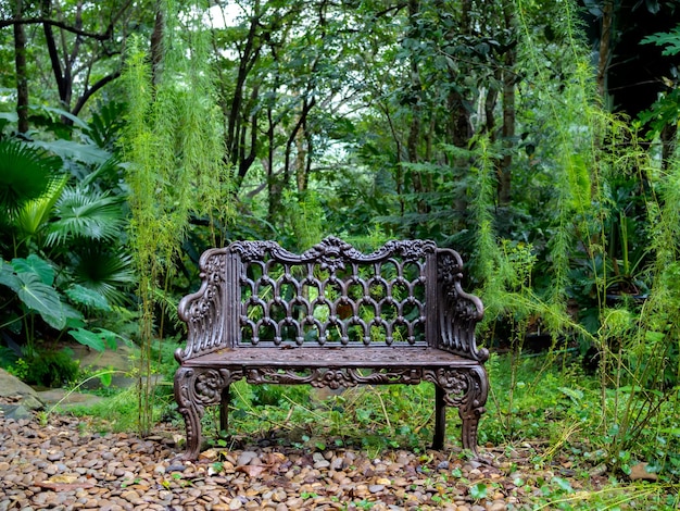 Empty old lonely vintage iron bench seat chair at the desolate yard on the green forest background