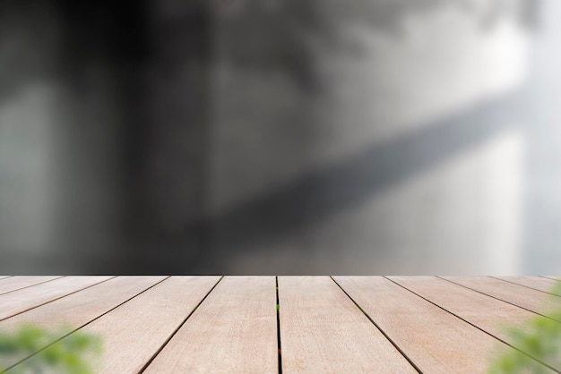 Empty old wooden table in front of blurred background of cement wall with shadow of leaf.