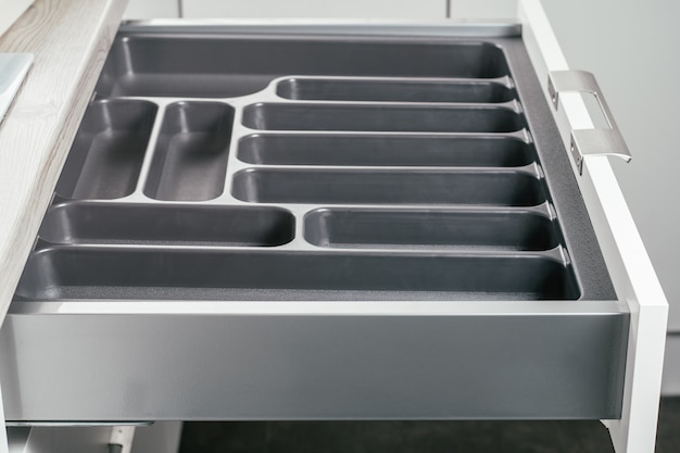 Empty open drawer of white kitchen set with black cutlery organizer tray, side view. Storage organization system