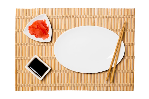 Empty oval white plate for sushi with chopsticks, ginger and soy sauce on bamboo mat