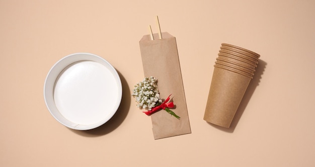 Empty paper plate for soup and brown cardboard cups on beige background top view