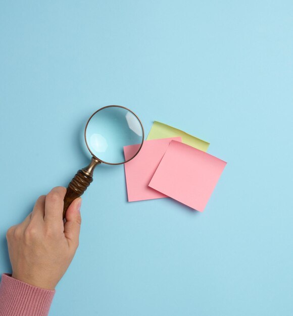 Empty paper stickers adhered to a blue background and a female hand with a magnifying glass