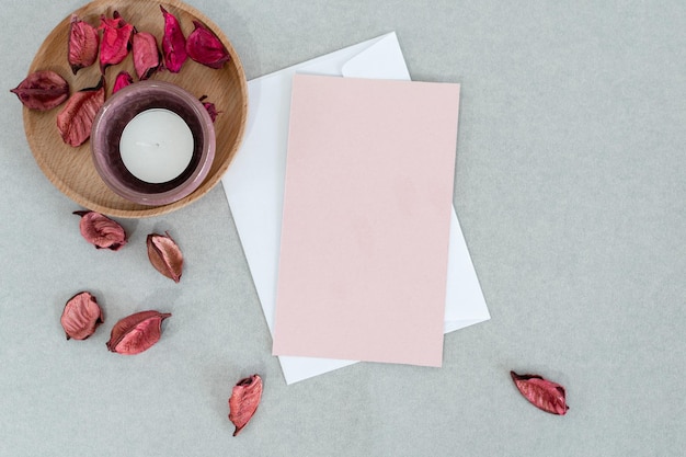 Empty pink card with white envelope candle and petals on gray background