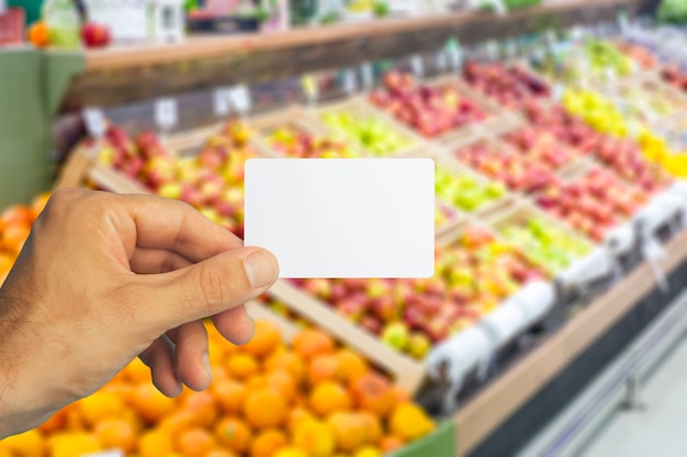 Empty plastic grocery card in hand on supermarket background grocery card for discounts and promotio...