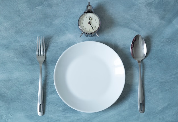 Empty plate and clock with spoon and fork for food. Lunchtime. 